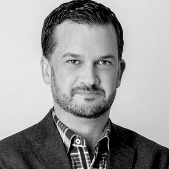 A man with a beard is wearing a suit and plaid shirt.
