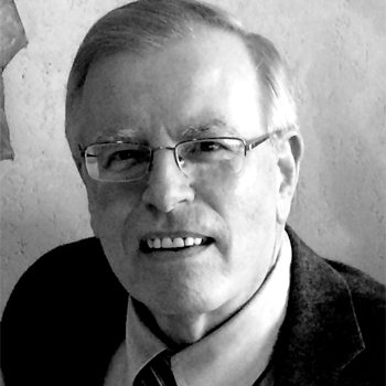 A man wearing glasses and a suit is smiling in a black and white photo