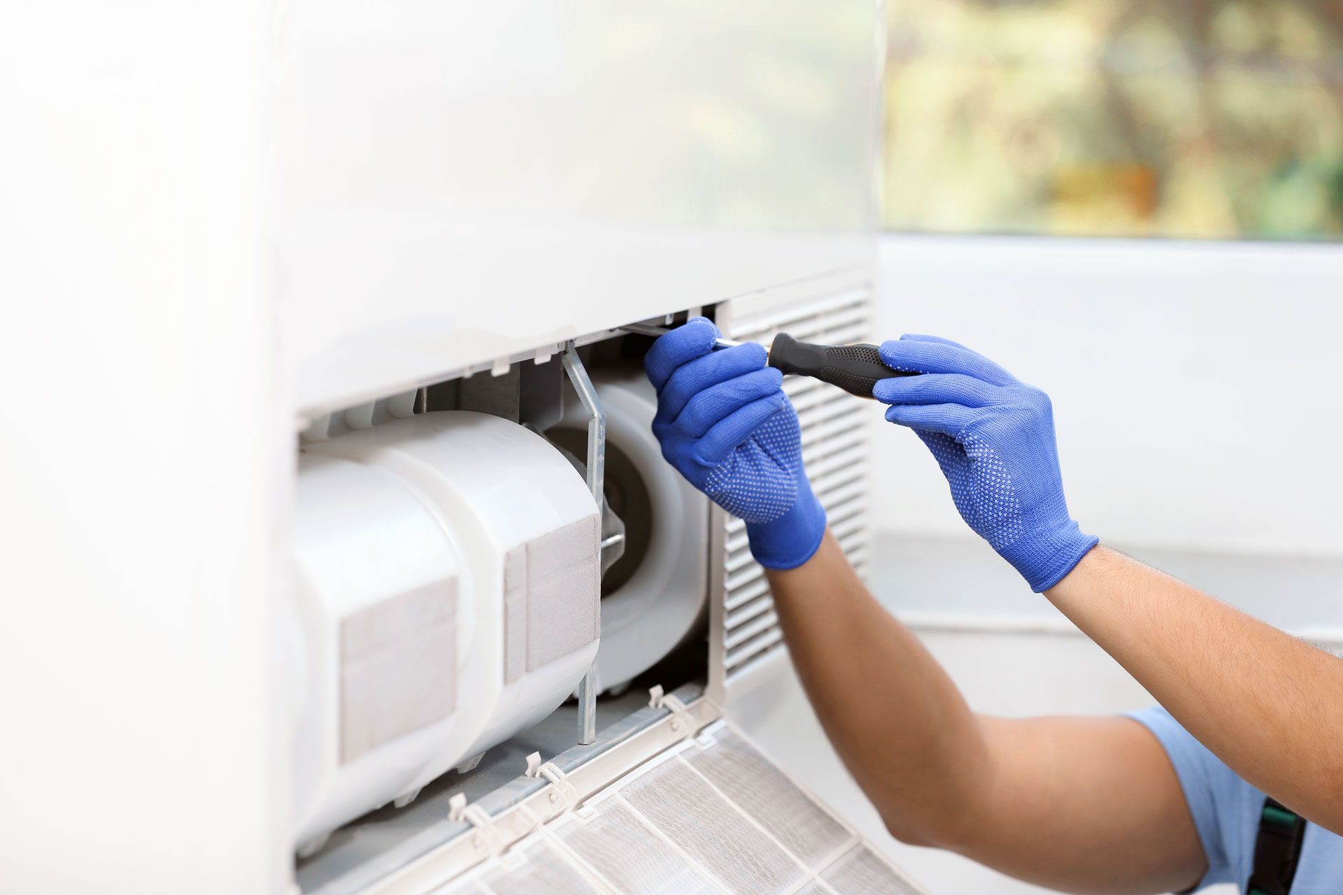 Person in blue gloves cleaning a white air conditioner.