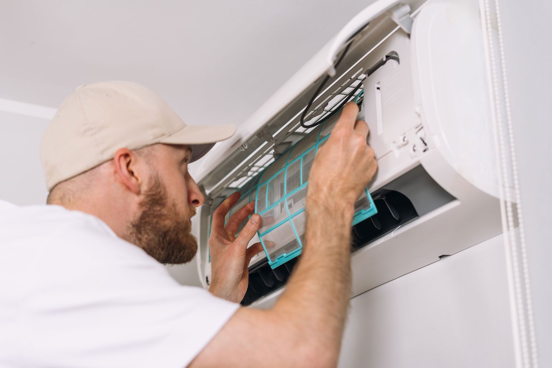 Man in cap cleaning an air conditioner filter.