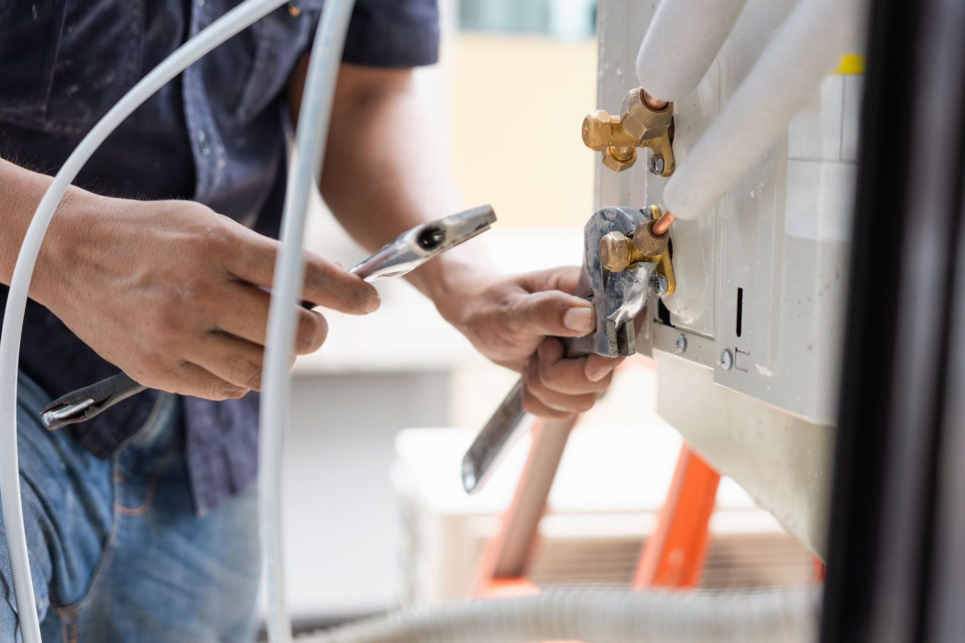Person using wrench to connect pipes to an air conditioning unit outside.