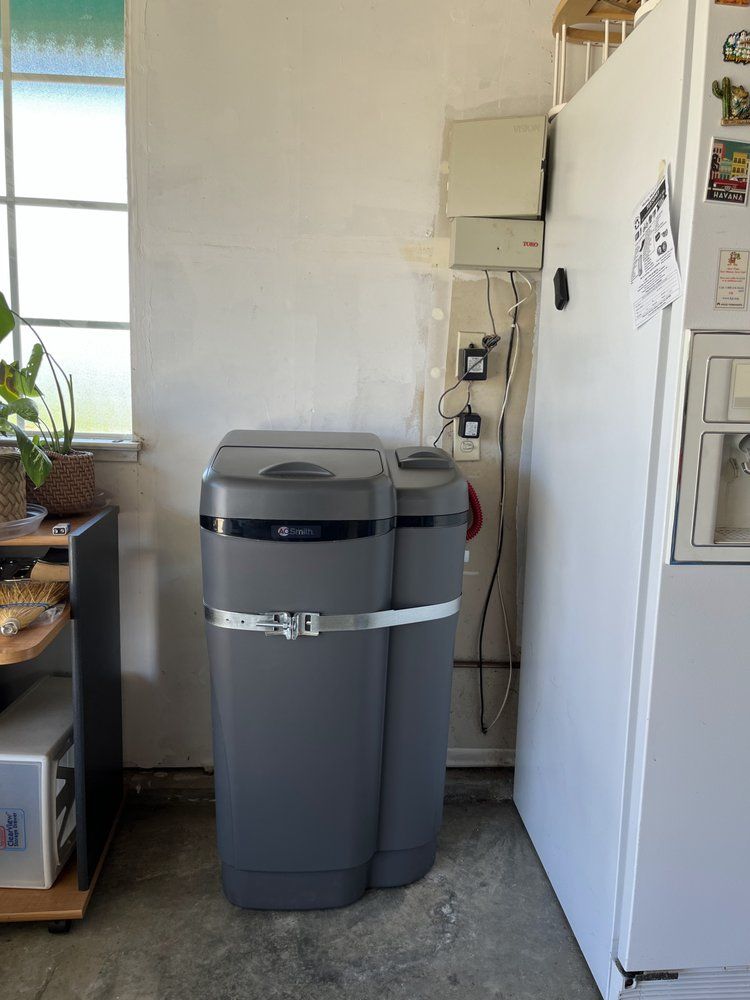 A gray water softener sits next to a white refrigerator