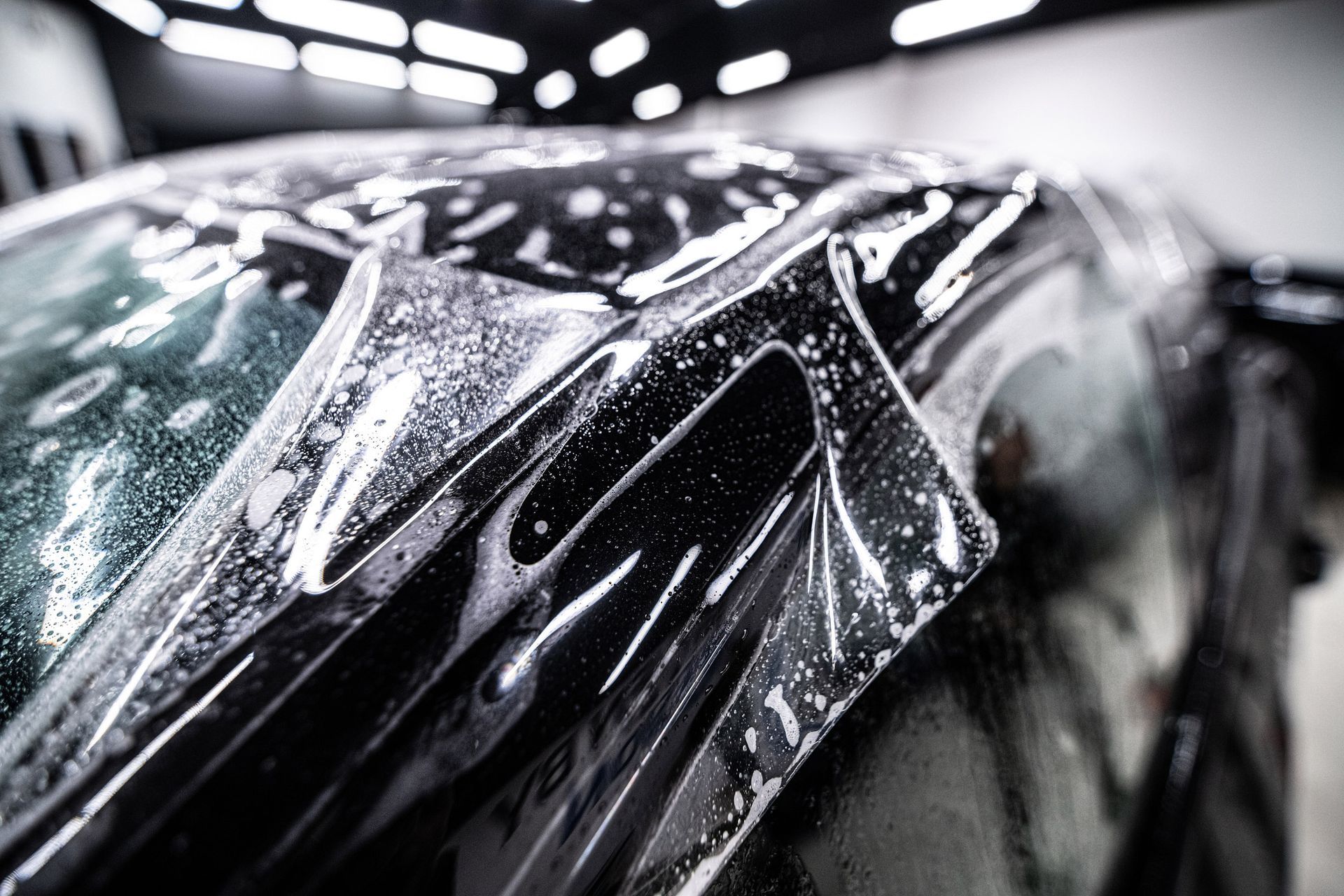 Car being wrapped in clear protective film, in a brightly lit garage.