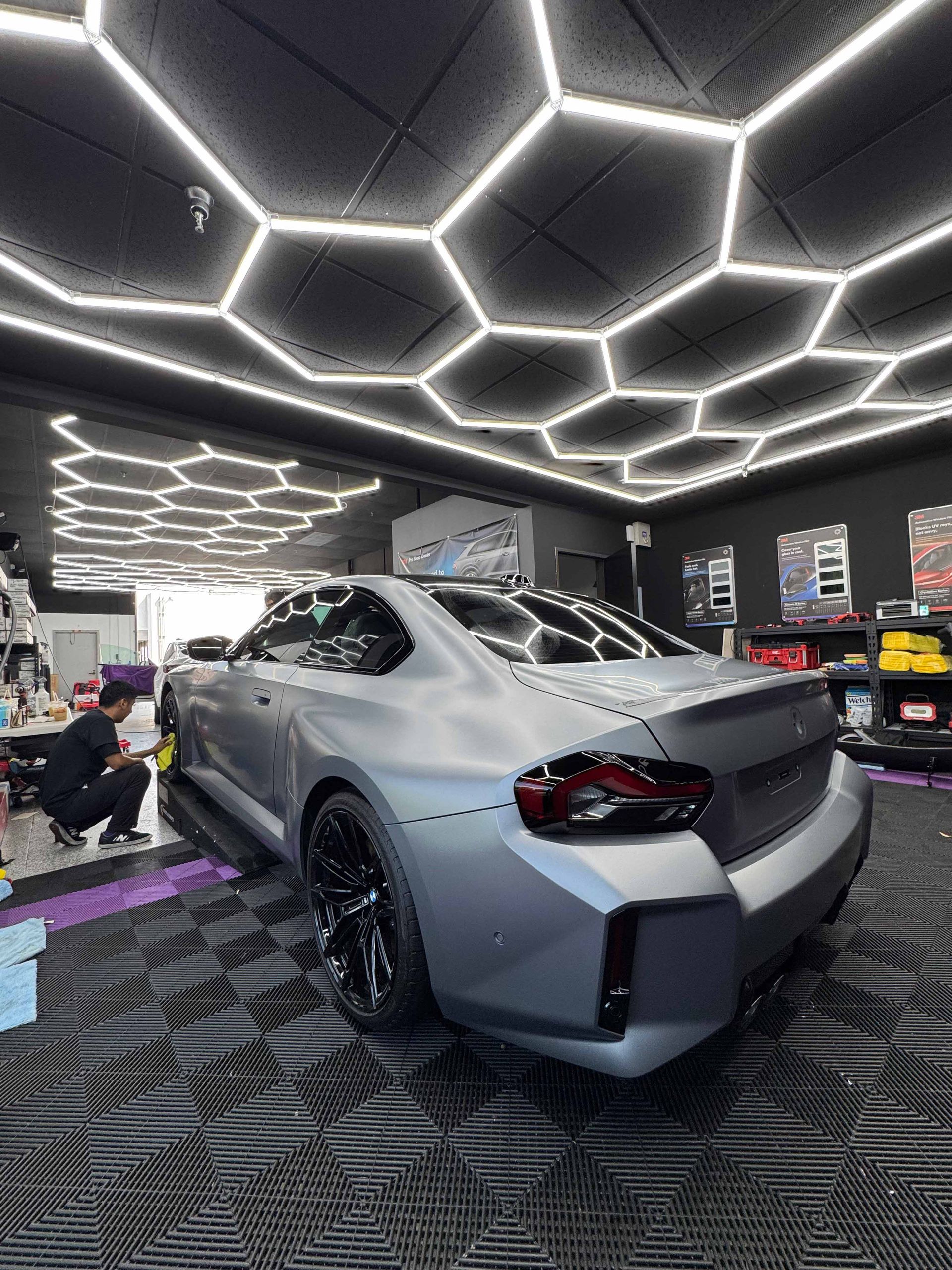 Person applying window tint film to a red car window, inside a well-lit shop.