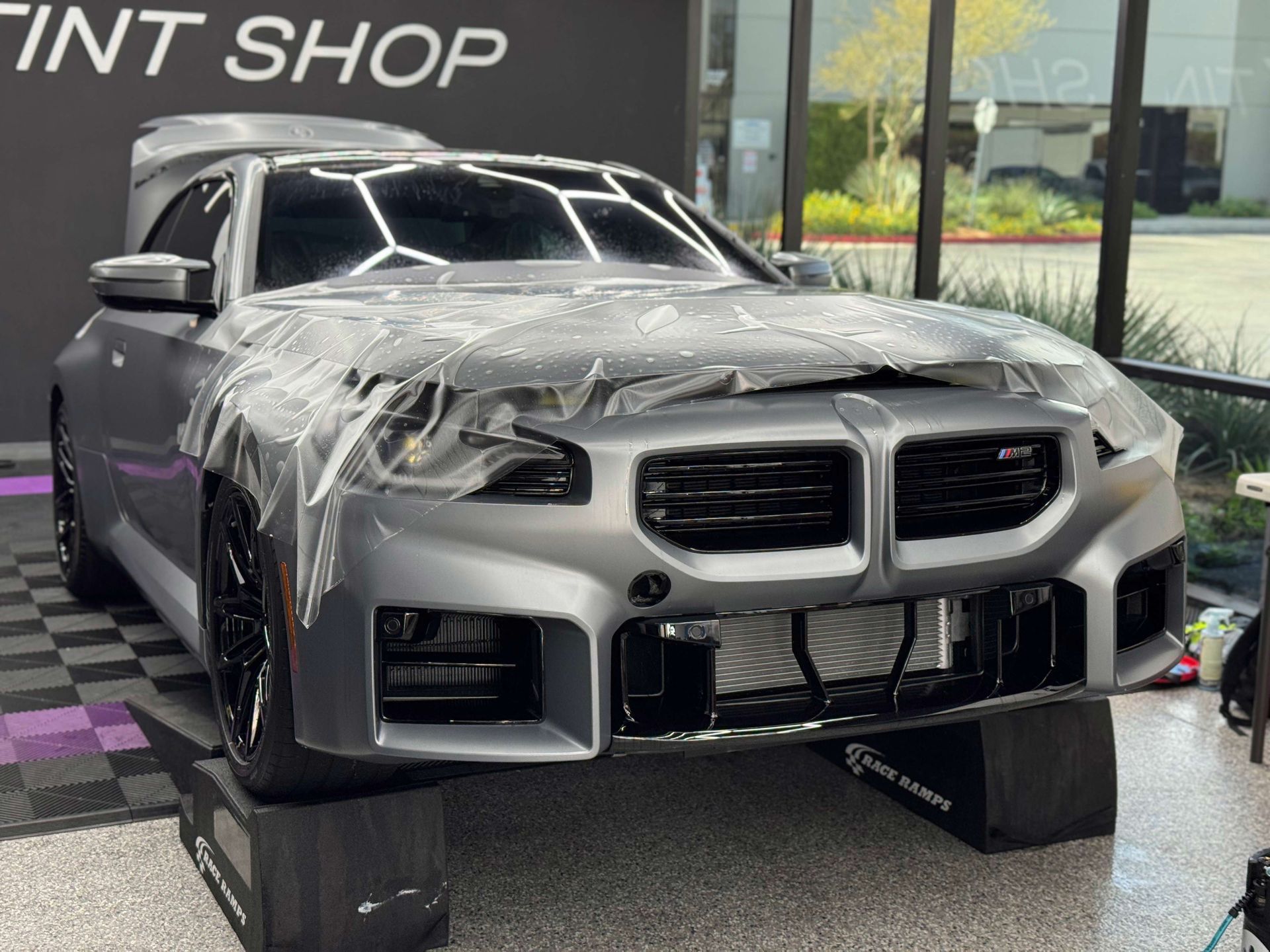 Gray BMW car with protective film in a tint shop, front view, hood open.