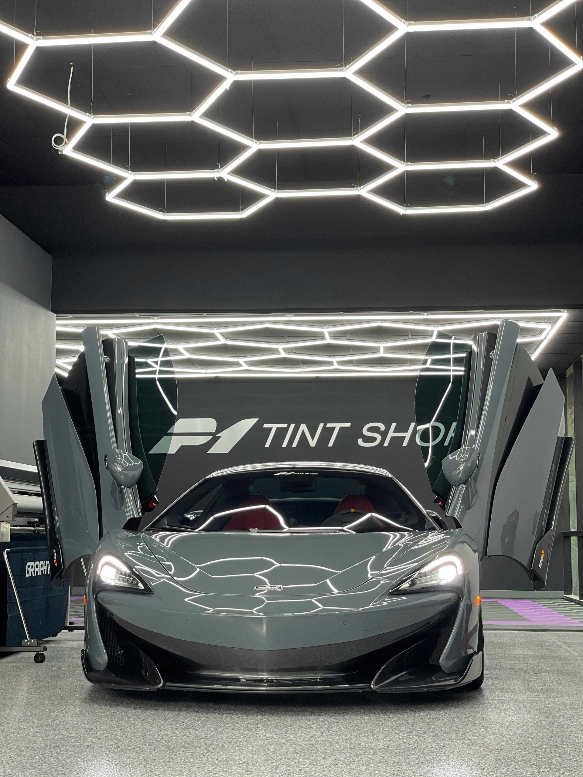 Gray McLaren with doors open, inside a shop, under honeycomb lights.