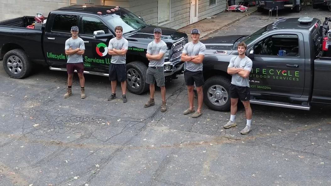 Five people stand in front of two black trucks, possibly a work crew.