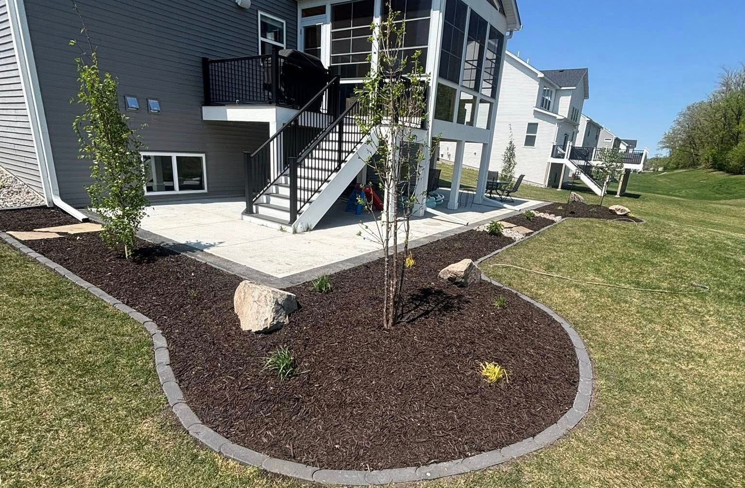 Backyard landscaping with dark mulch, stone edging, and a gravel patio next to a house.