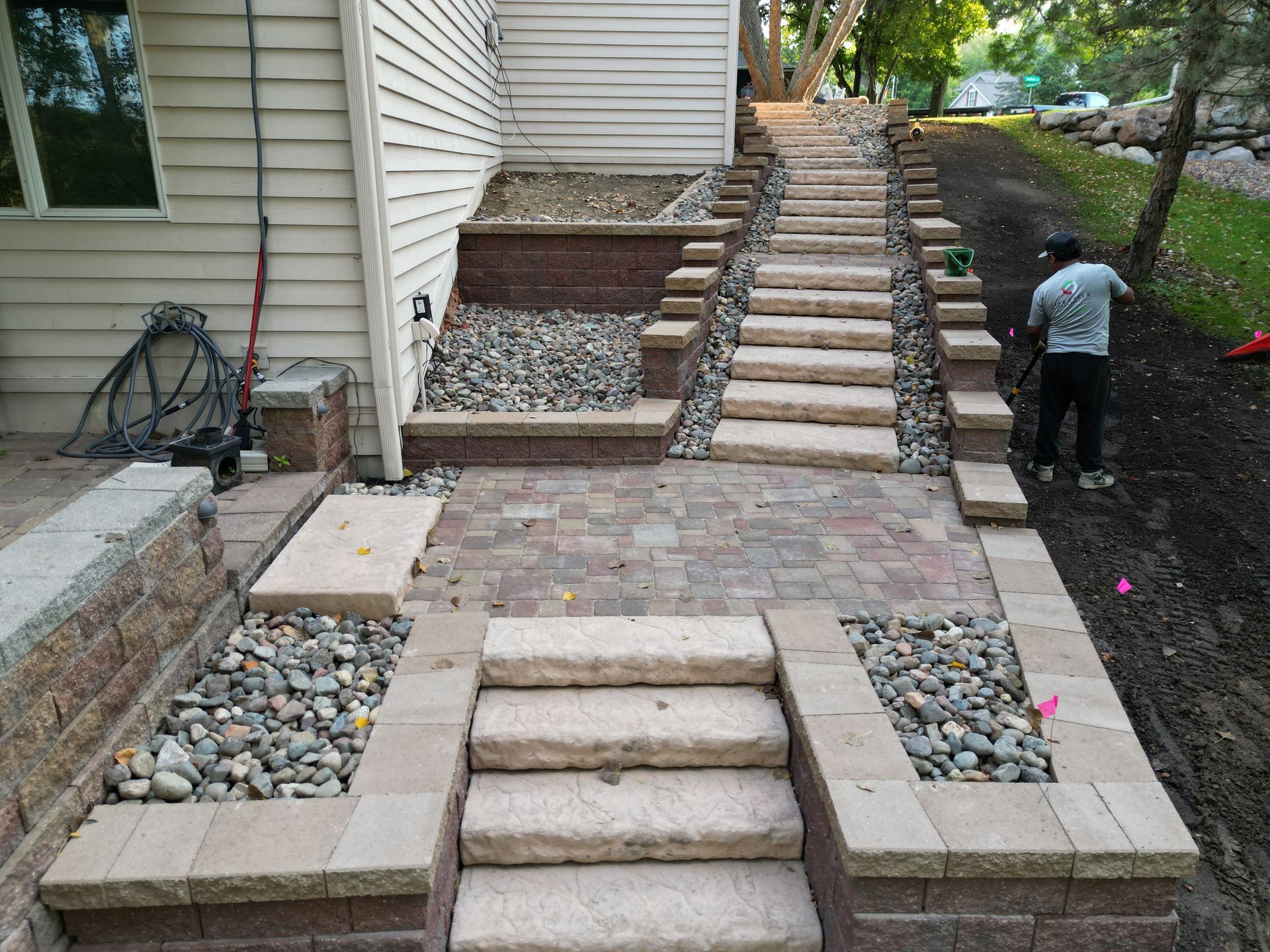 Stone steps and walkway leading uphill next to a house; person working on the side.