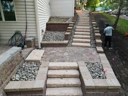 Stone steps and walkway leading uphill next to a house; person working on the side.