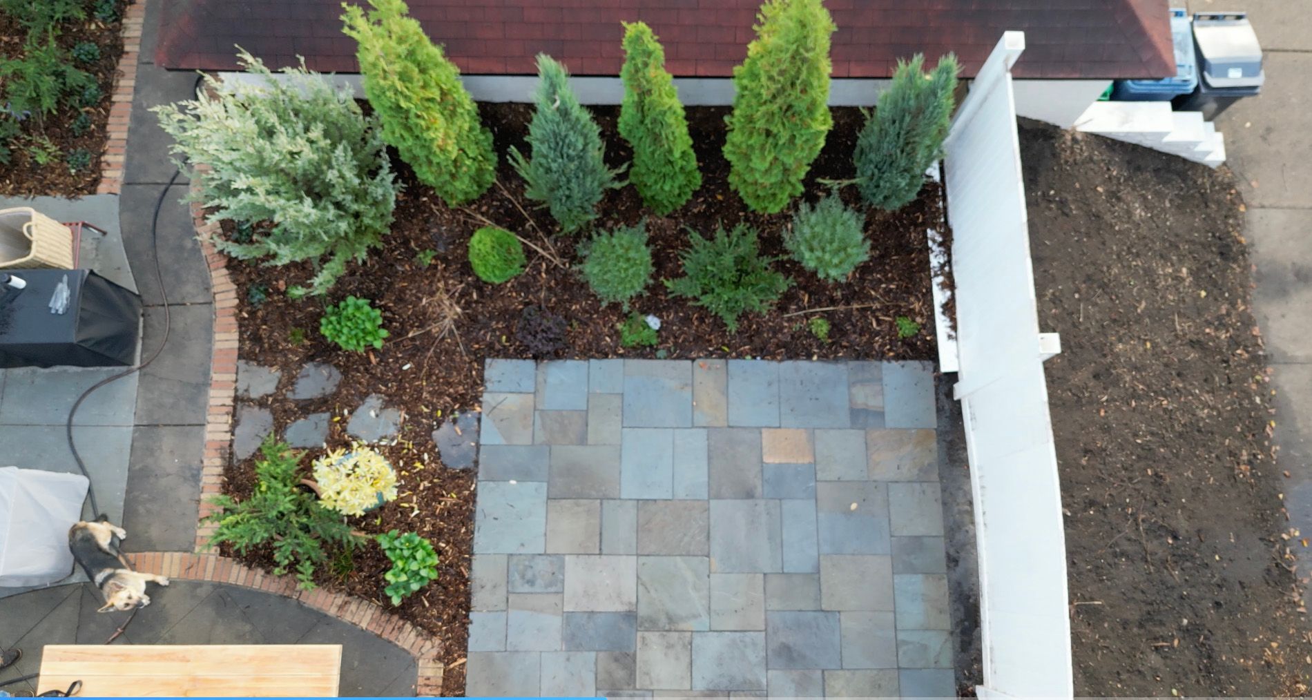Overhead view of a landscaped backyard with a patio, garden beds with plants, and a white fence.