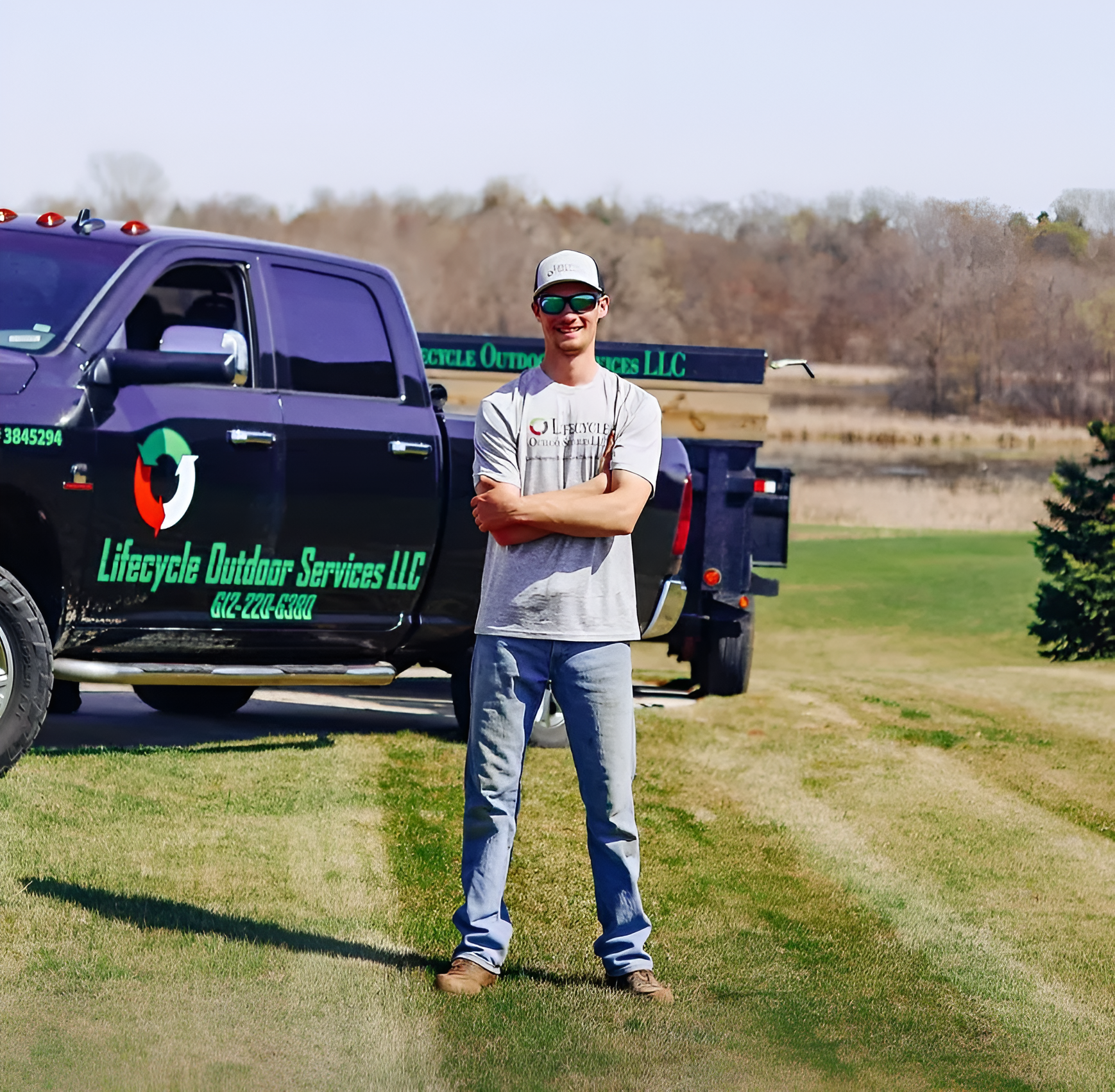 Man standing with arms crossed in front of a dark truck with Lifecycle Outdoor Services LLC logo.