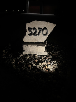 Illuminated address marker with the number 5270 on a stone base surrounded by rocks.