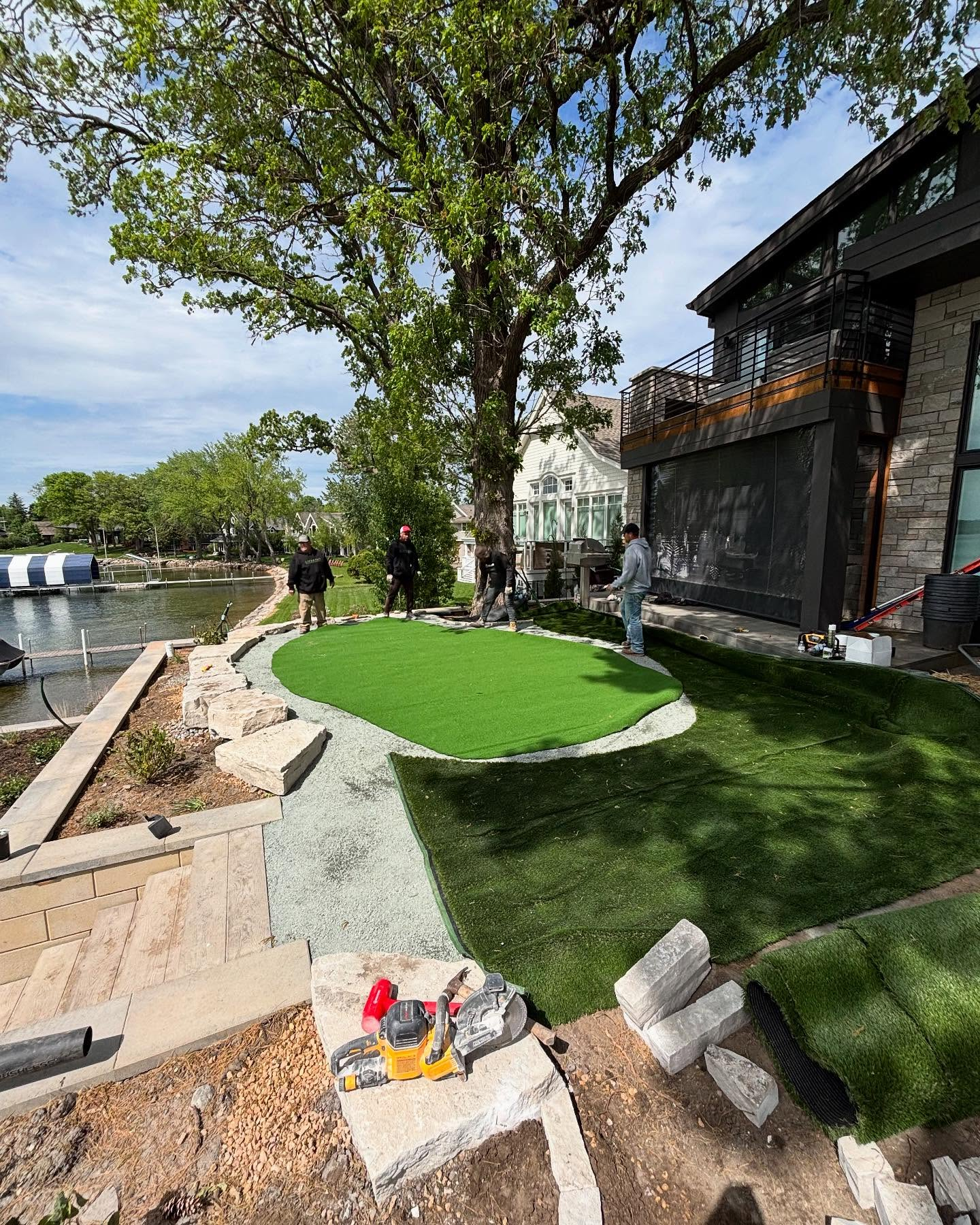 Golf green installation near a lake. Workers install artificial turf next to a home with a balcony.
