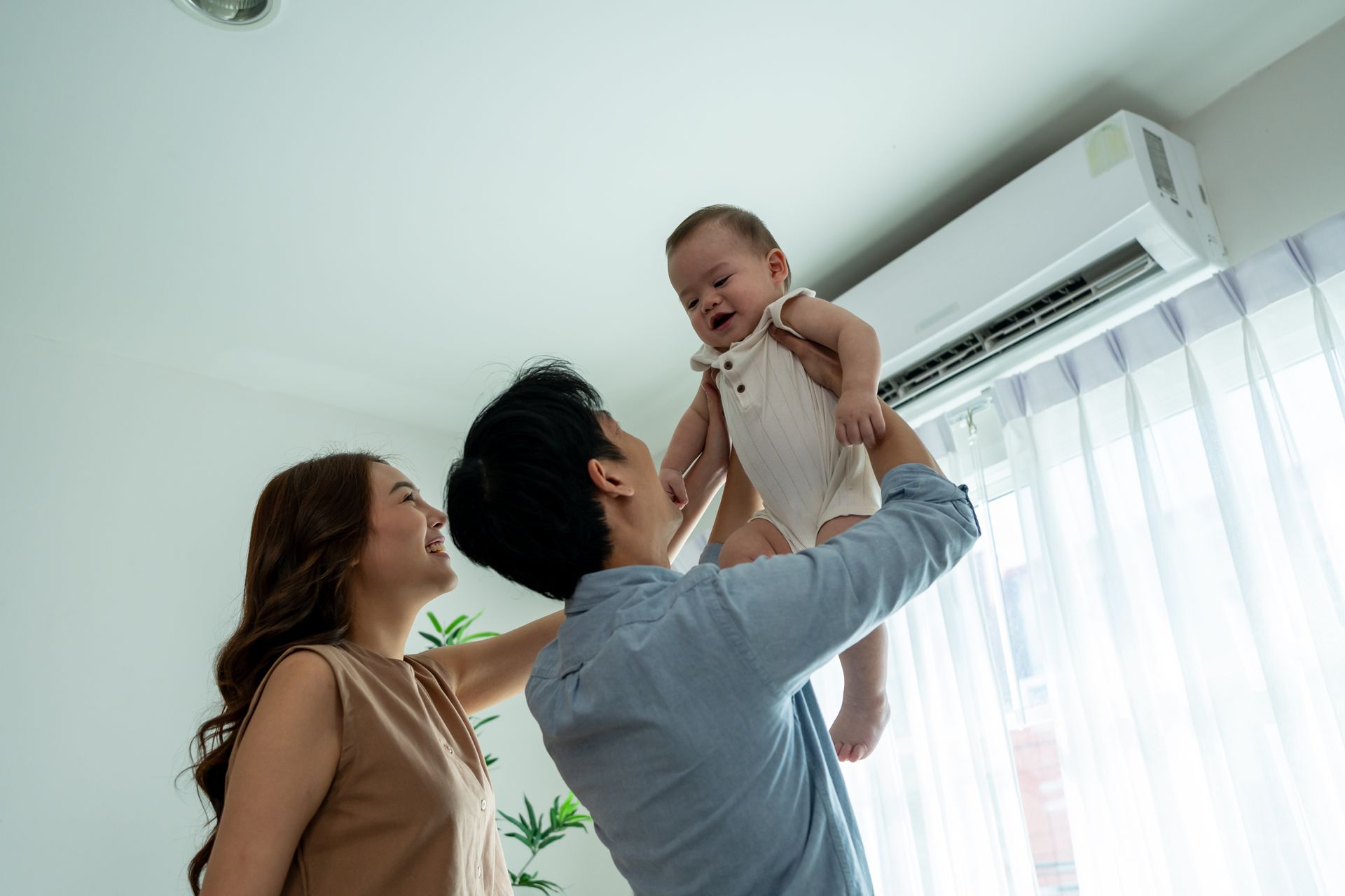 Family lifting a smiling baby near a bright window in a living room
