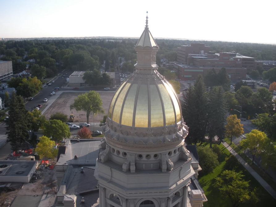Dining room with wooden table, beige chairs, and glass-paneled door. Sunlight streams through the window.