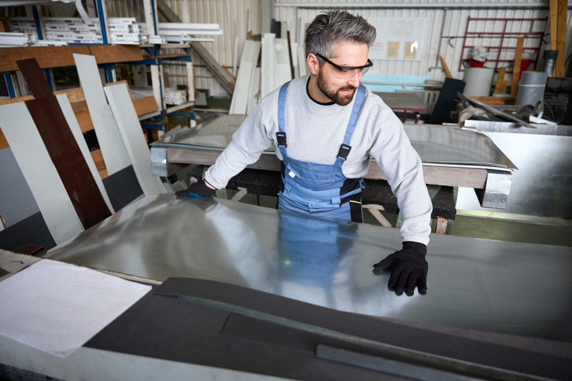 Worker in blue overalls handling large metal sheets in a workshop