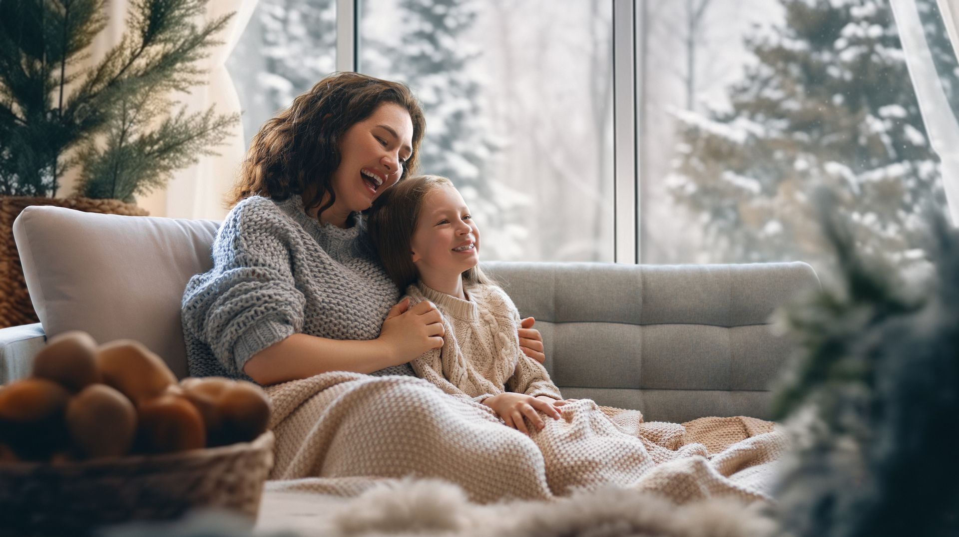 Woman and child sitting on a couch, reading together in a cozy living room by a window.