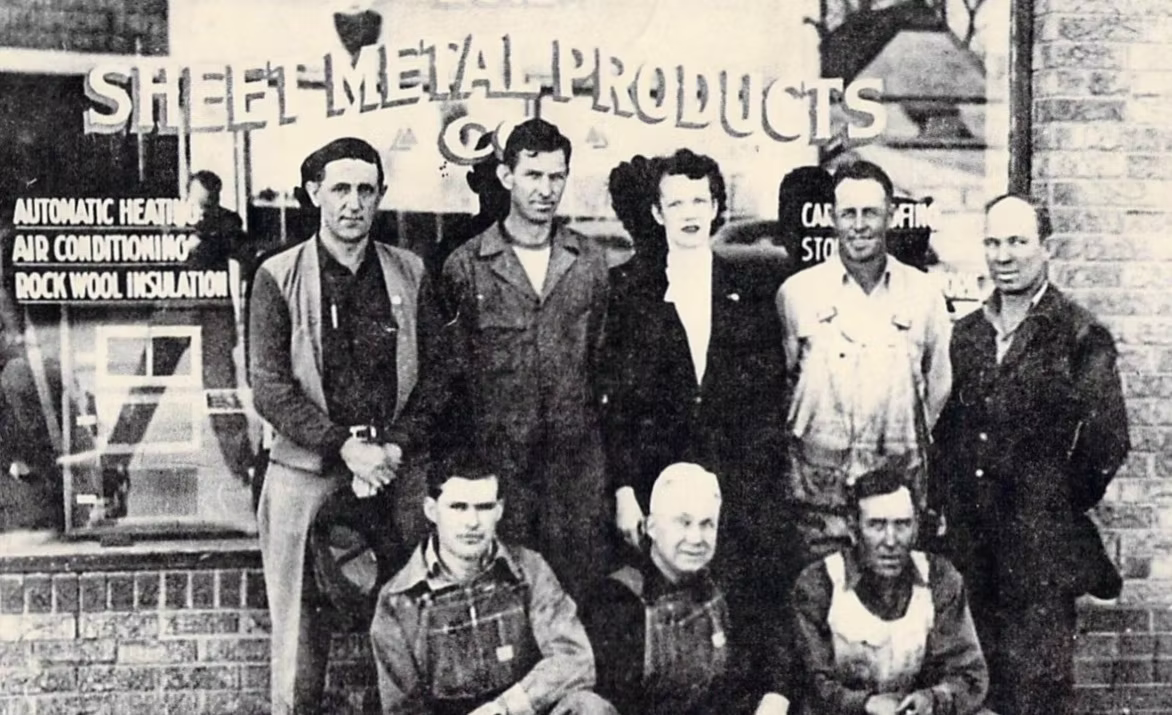 Brick building with a white steeple topped by a teal spire against a light blue sky.