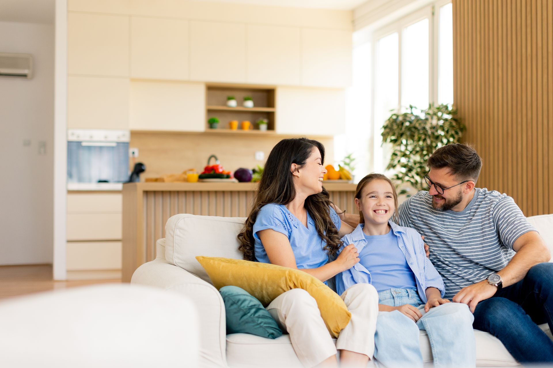 Family sitting on a couch in a bright living room, smiling and chatting together