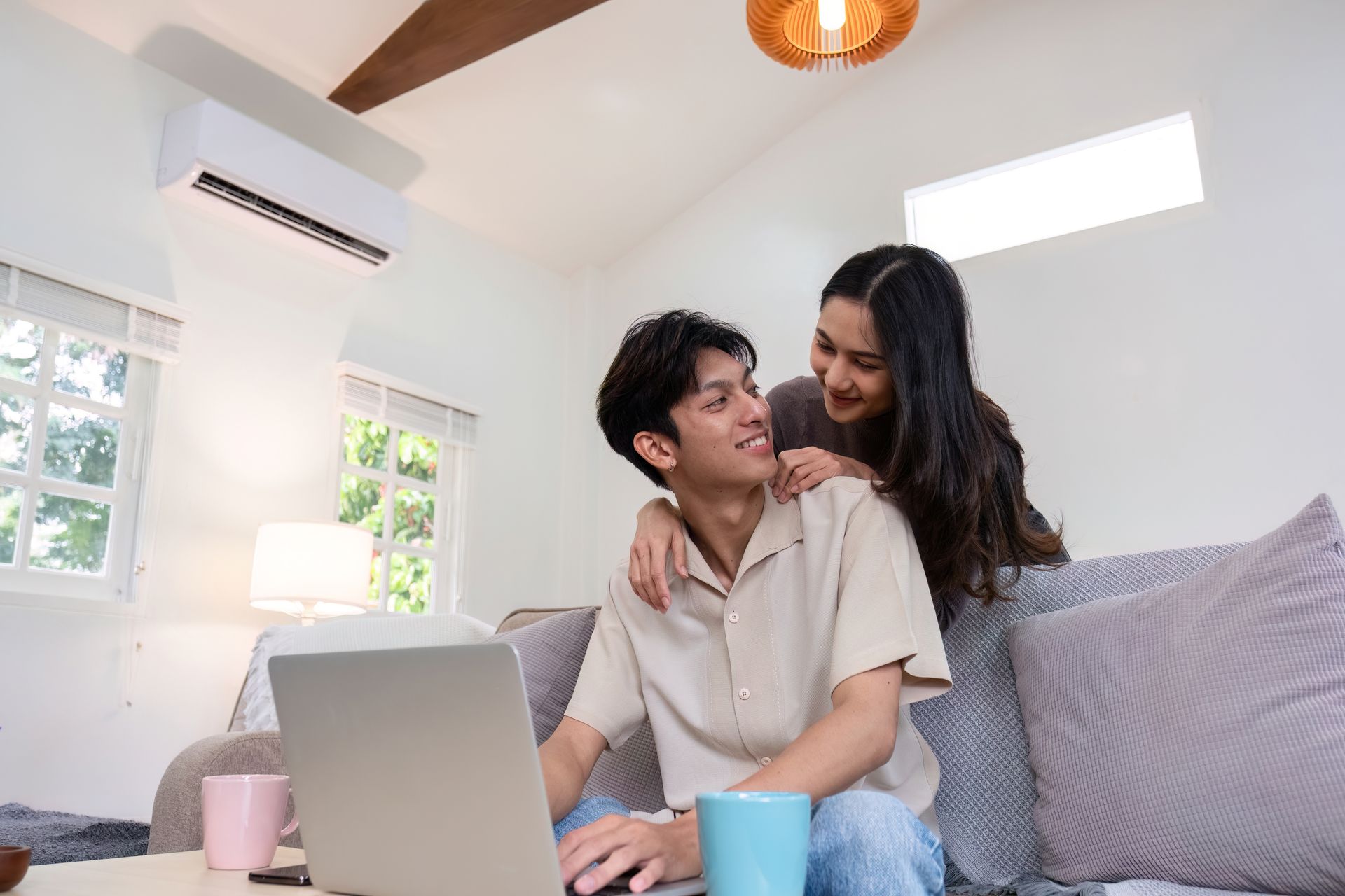 Two people smiling on a couch with a laptop, in a bright living room