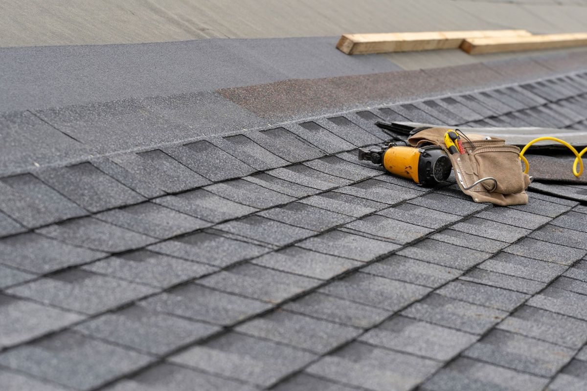 Roof Repairs — Toolbelt with Nail Gun Lying on Asphalt Shingles in North Bergen, NJ