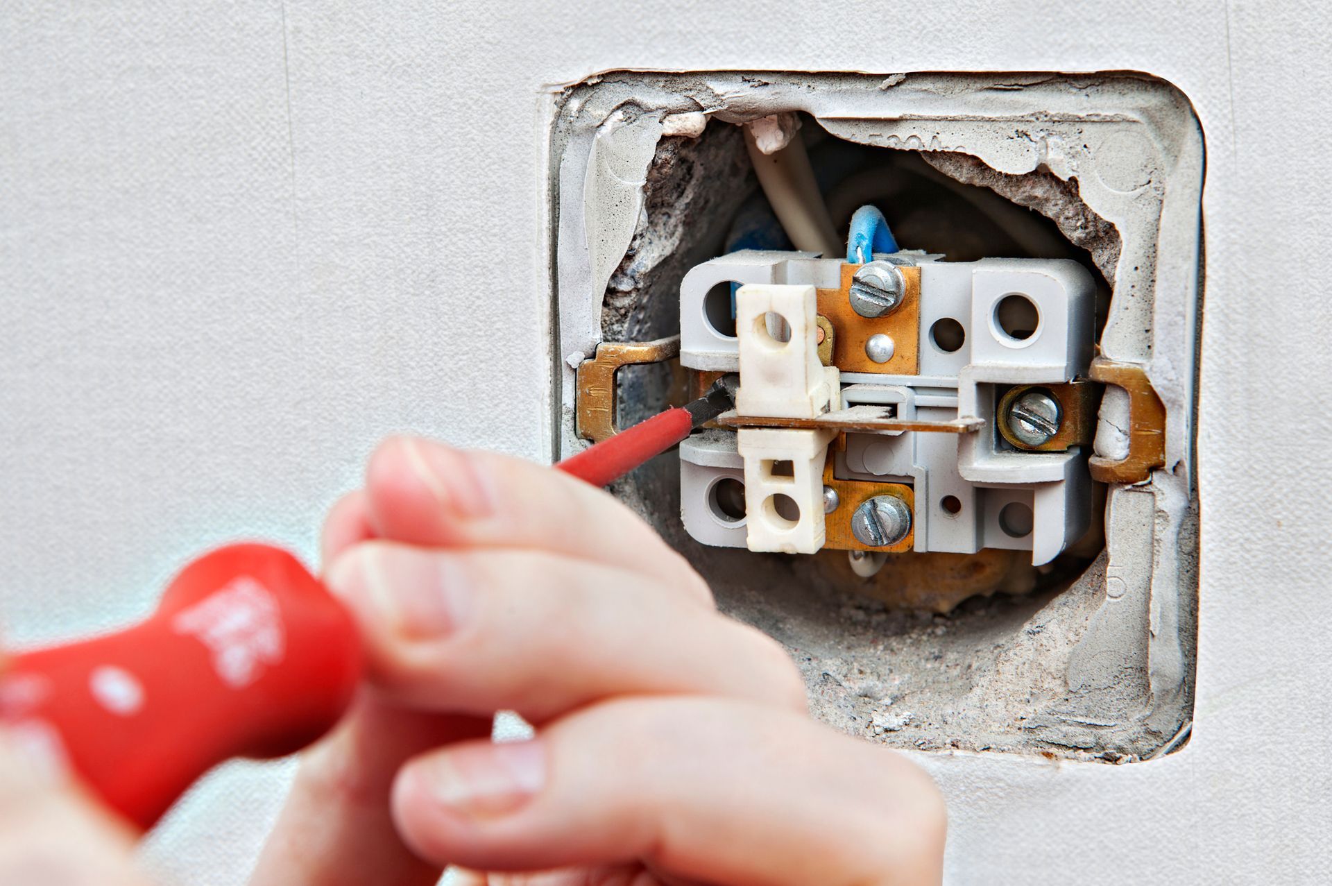 A person is fixing a light switch with a red screwdriver