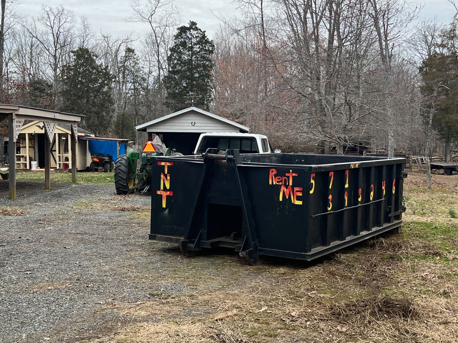 a dumpster is parked in a gravel lot in front of a house .