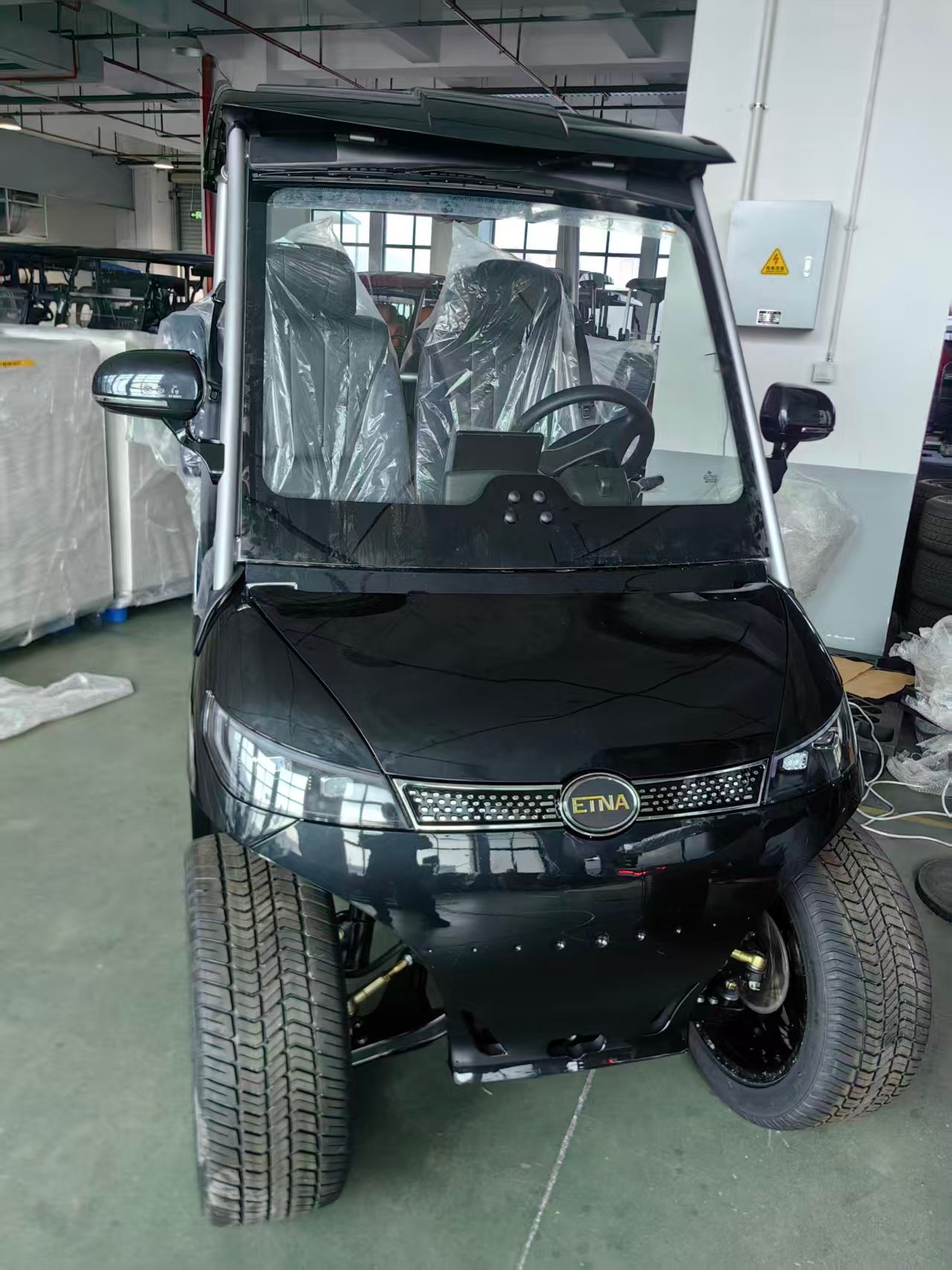 Black electric golf cart with windshield, roof, and headlights, indoors.