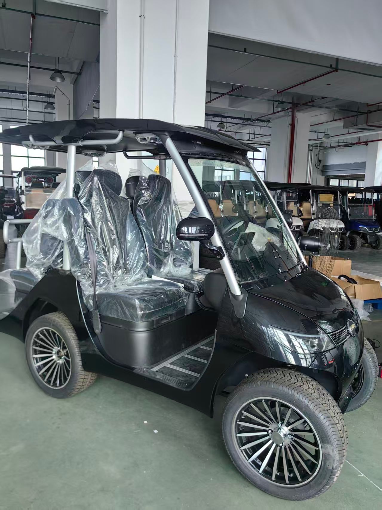 Black electric golf cart with windshield, roof, and headlights, indoors.