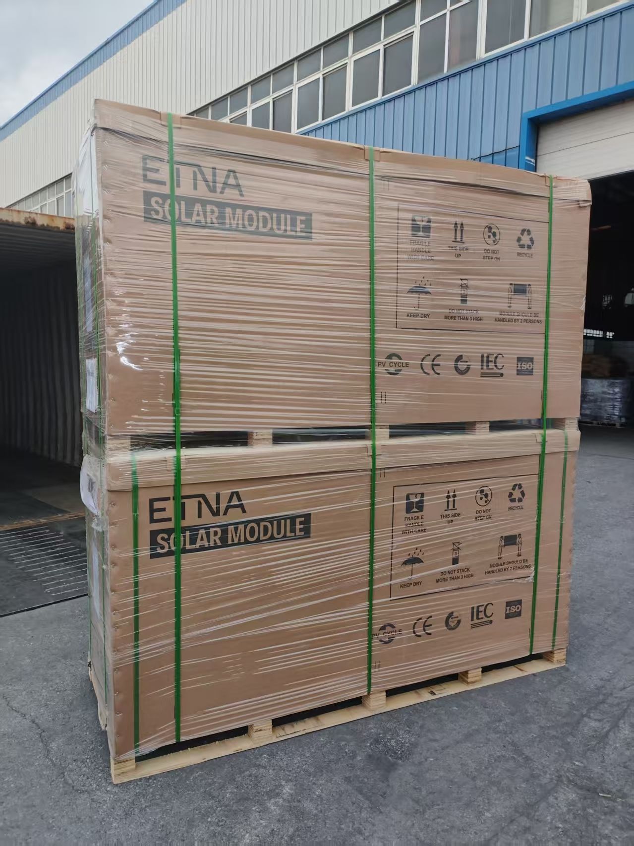 Two pallets of ETNA Solar Modules, wrapped in plastic, stacked outside a building.