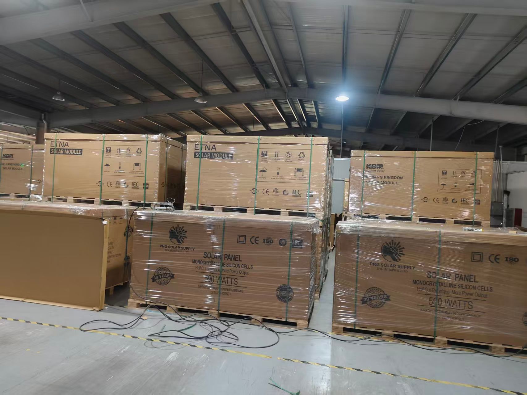 Two pallets of ETNA Solar Modules, wrapped in plastic, stacked outside a building.