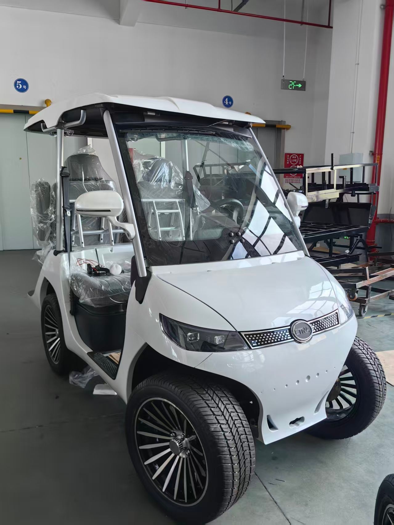 White golf cart with black wheels, parked indoors.