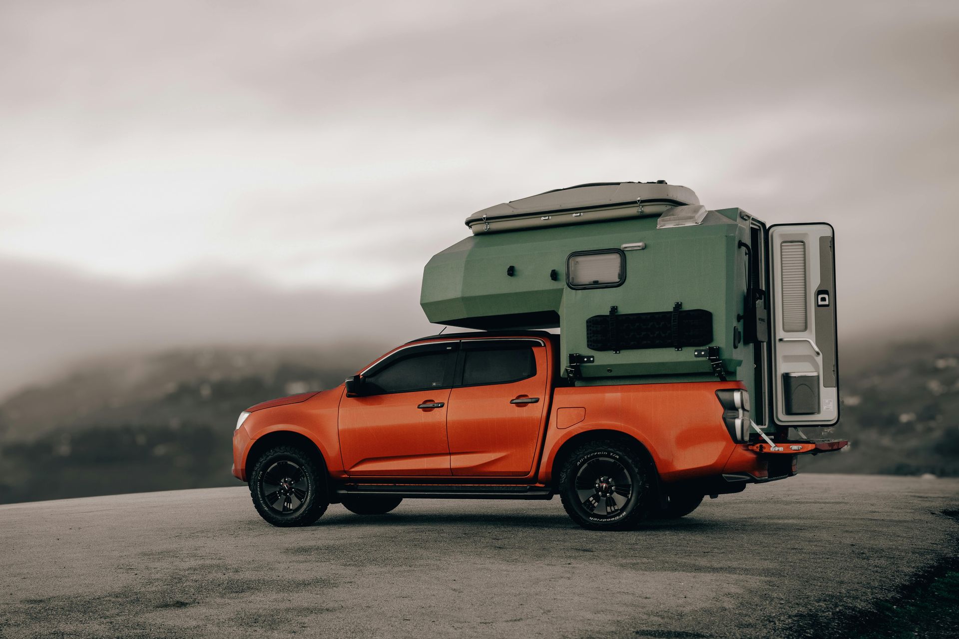 Orange pickup truck with a green camper shell on a mountain.