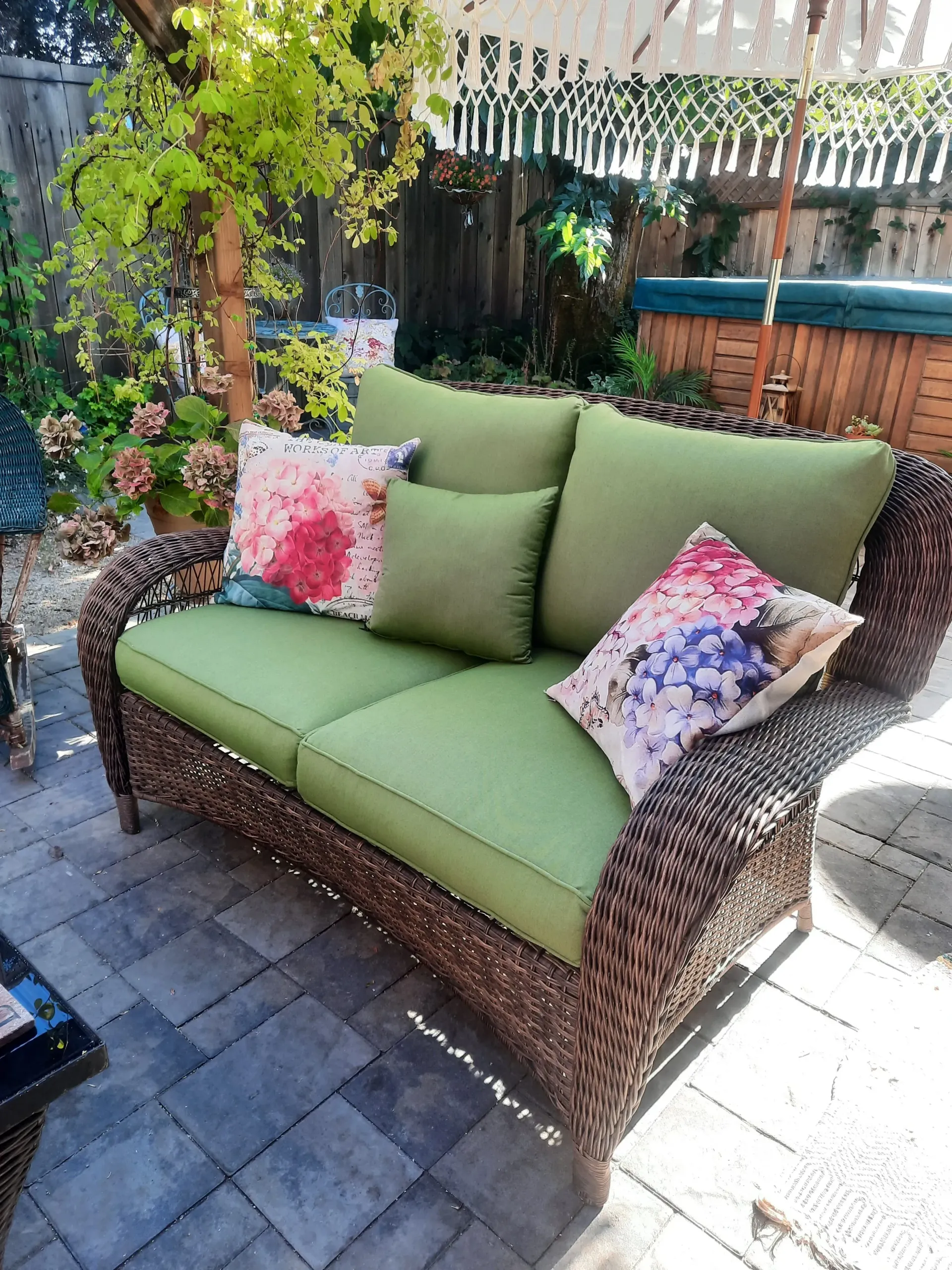 A wicker couch with green cushions and pillows on a patio.