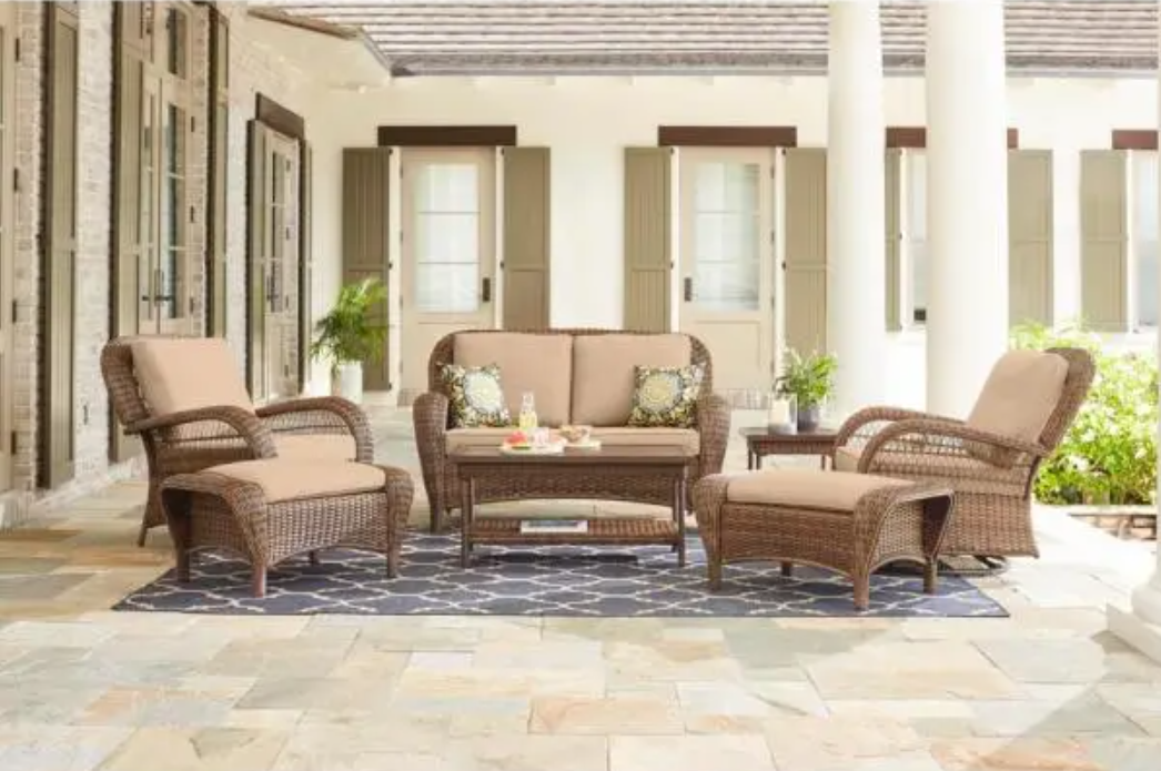A patio with a couch , chairs , ottoman and table.