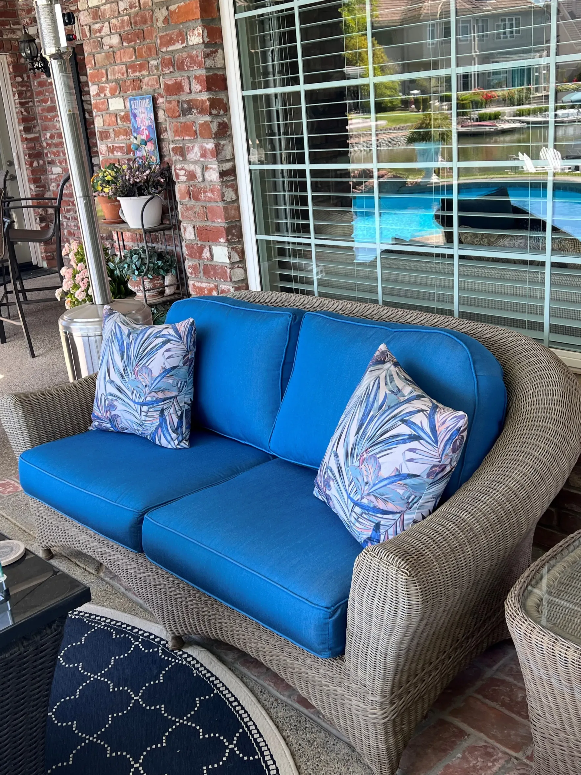 A wicker couch with blue cushions is sitting on a patio next to a window.