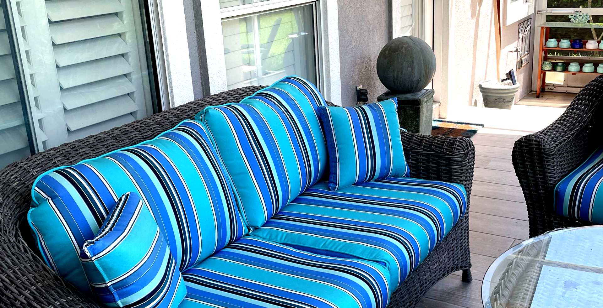 A wicker couch with blue and white stripes on it is on a porch.