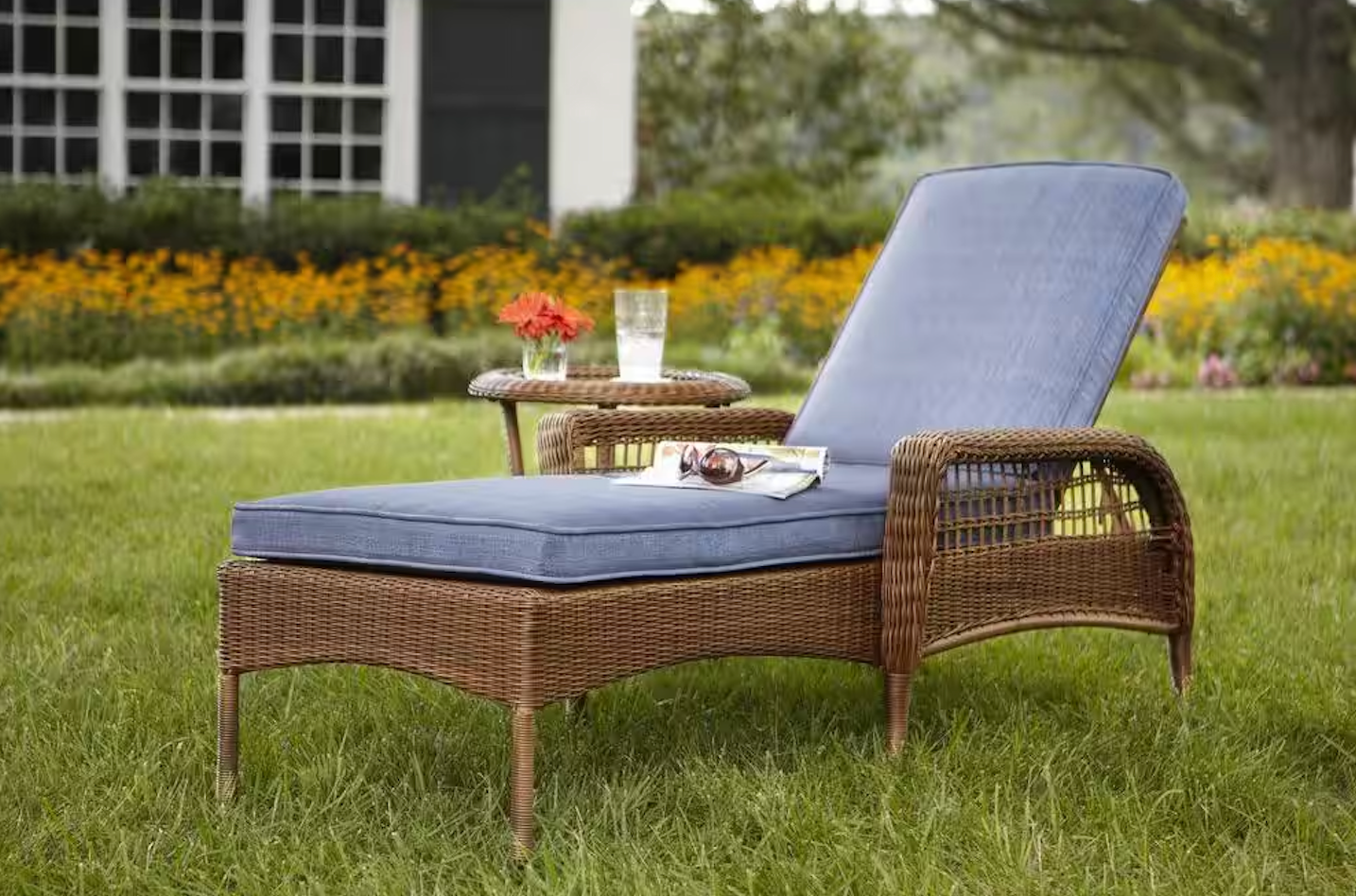 A wicker lounge chair from the Charlottetown Patio Furniture Collection with a blue custom cushion sitting in a yard with luscious green grass