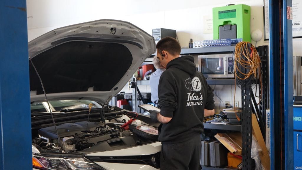 A man is working on a car in a garage with the hood open.