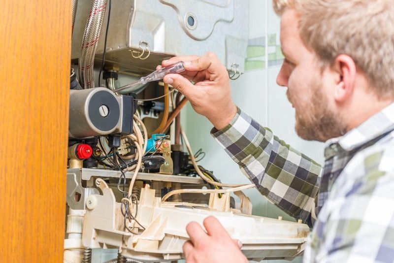 A man is fixing a boiler with a screwdriver.