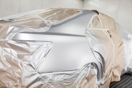 Car's side panel covered with plastic sheeting in a body shop, ready for painting.