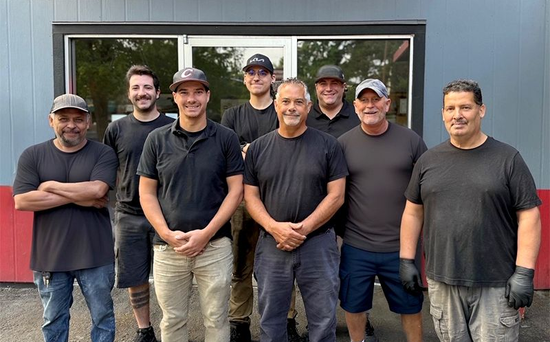Group of eight people standing outside a building; most wearing dark shirts and hats.