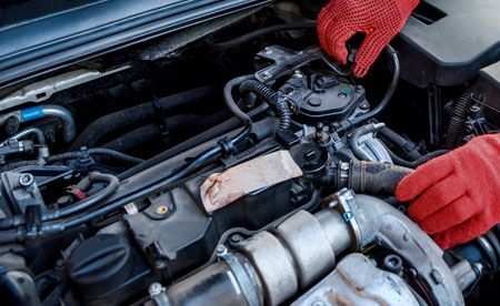 Hands in red gloves working on a car engine, inside a vehicle.