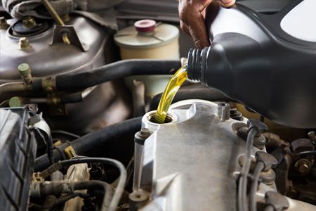 Filling engine oil into a car's engine; a person pours oil from a black container.