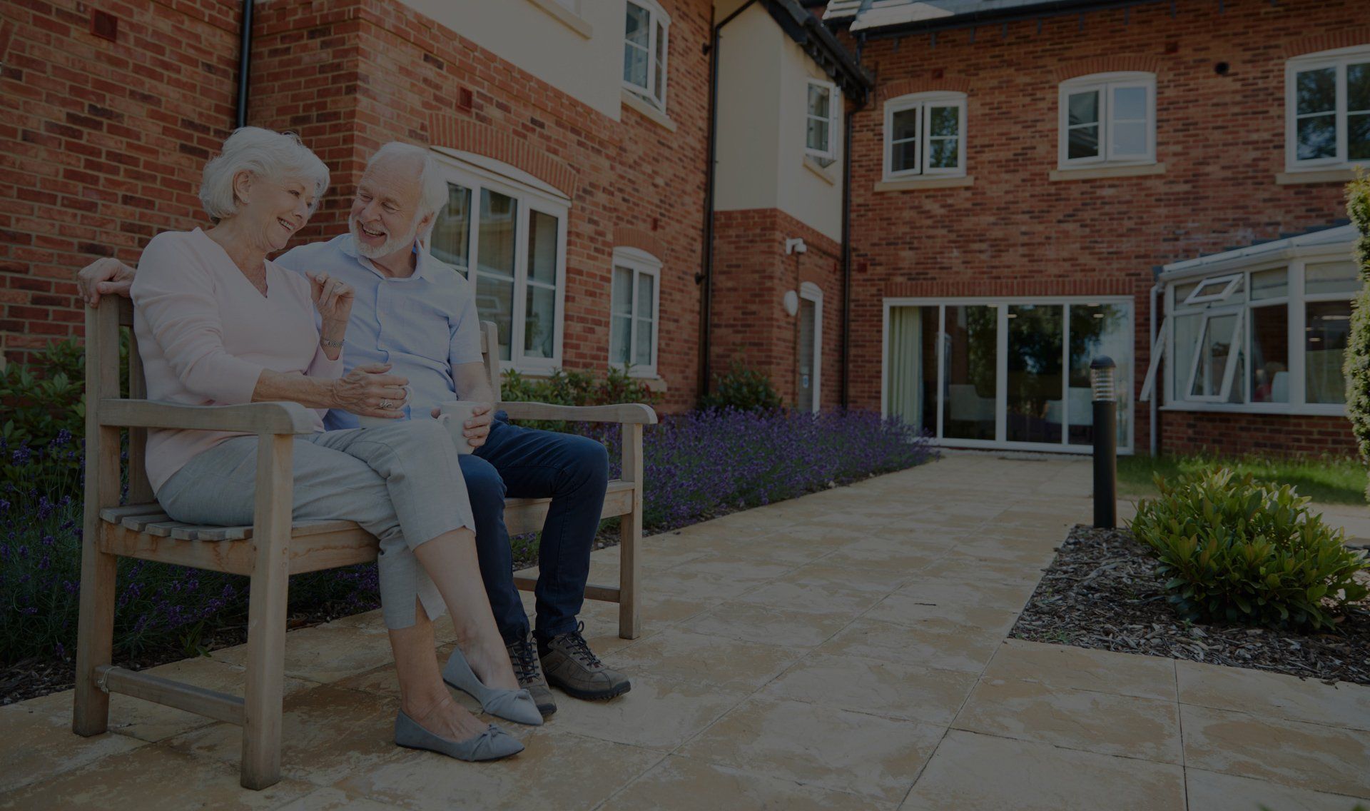 Elderly couple sitting on a bench, smiling, in front of a brick building. Elderly couple sitting on a bench, smiling, in front of a brick building.