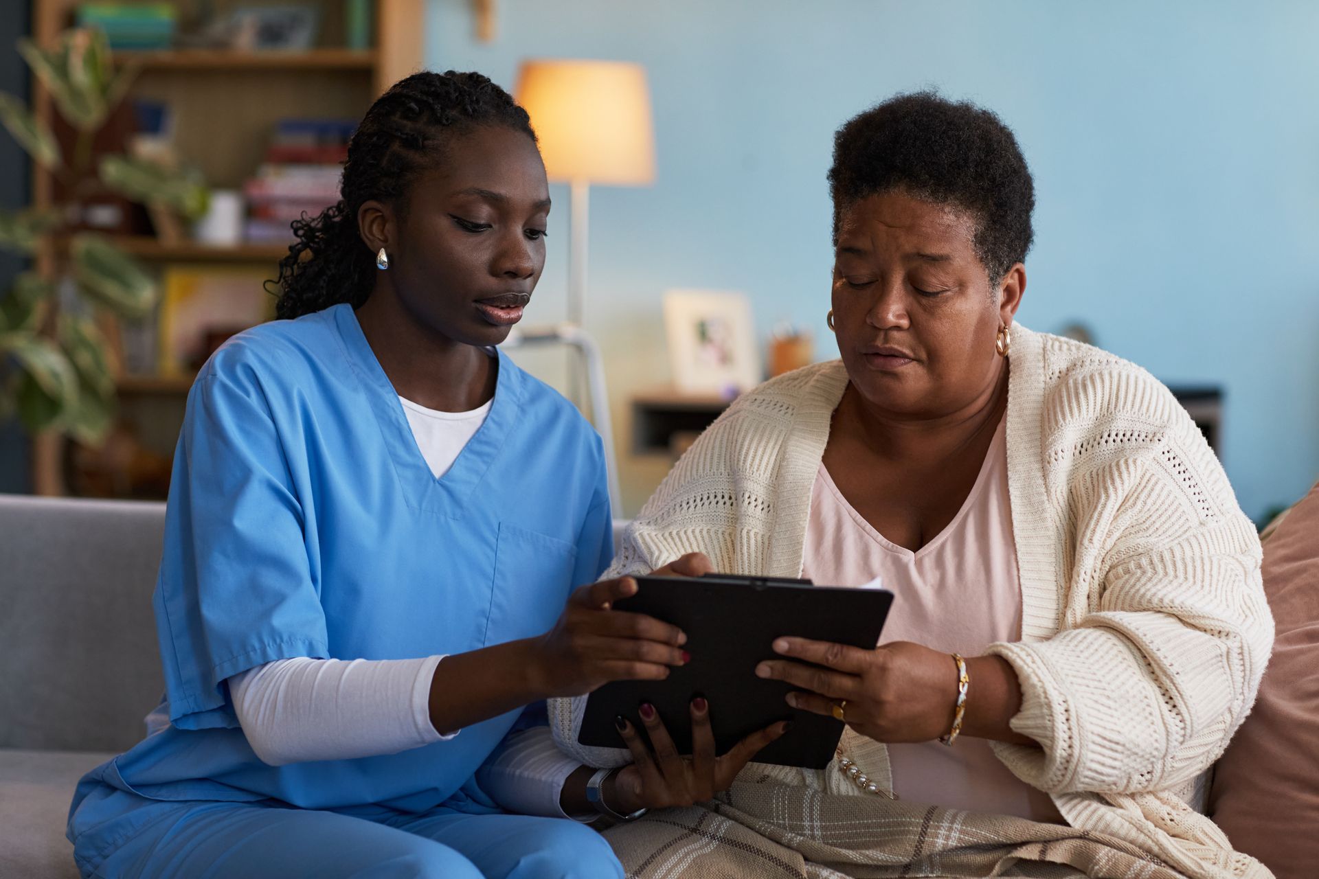Woman with hand on knee, consulted by nurse with clipboard, indoors.