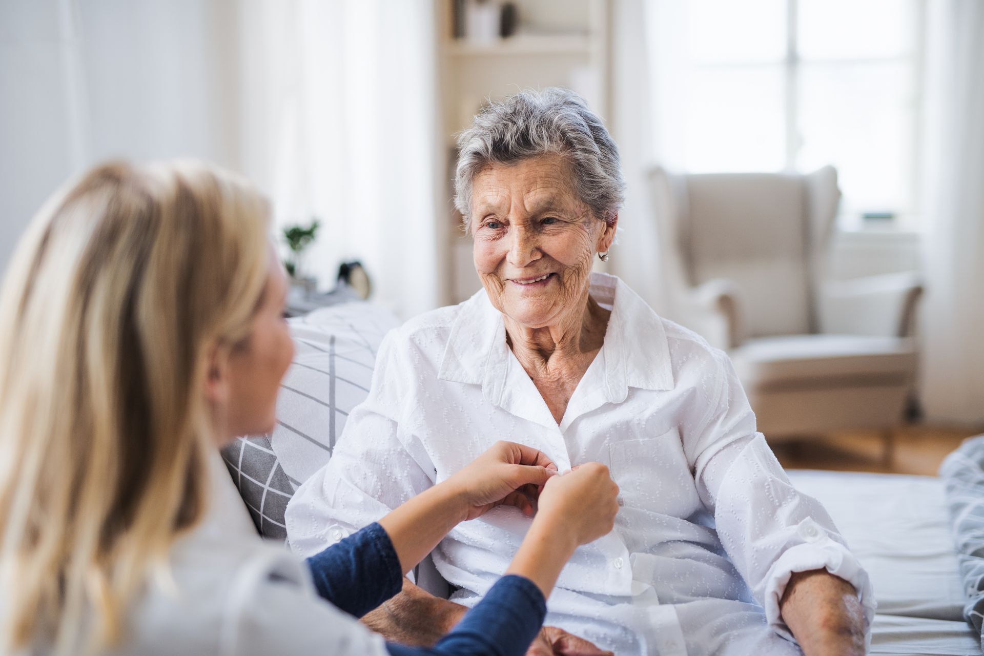 A woman is dressing a senior woman.