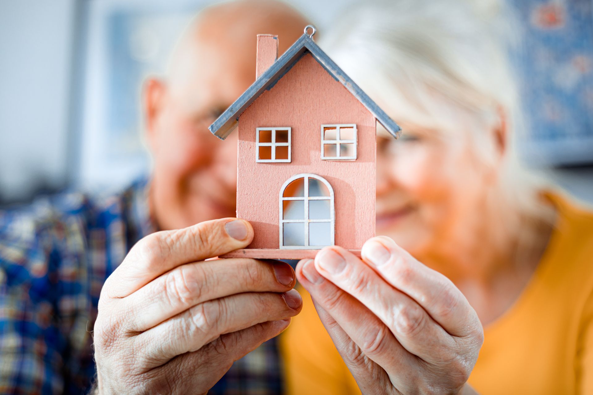 Senior hands holding a toy house to represent elder home security and retirement living.
