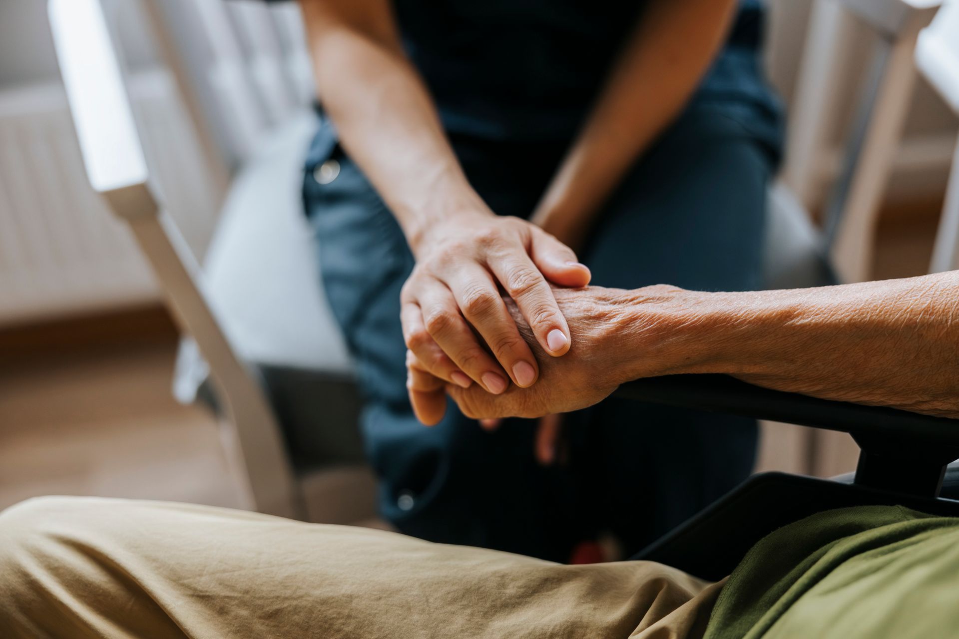Elderly person sitting in a chair, smiling, arms crossed. Yellow tulips in vase in foreground.